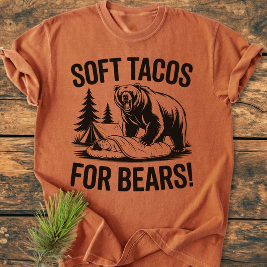 Soft Tacos For Bears - Vintage Wash Tee featuring a roaring bear illustration over a sleeping camper, with SOFT TACOS FOR BEARS! text, laid flat on a textured wood background.