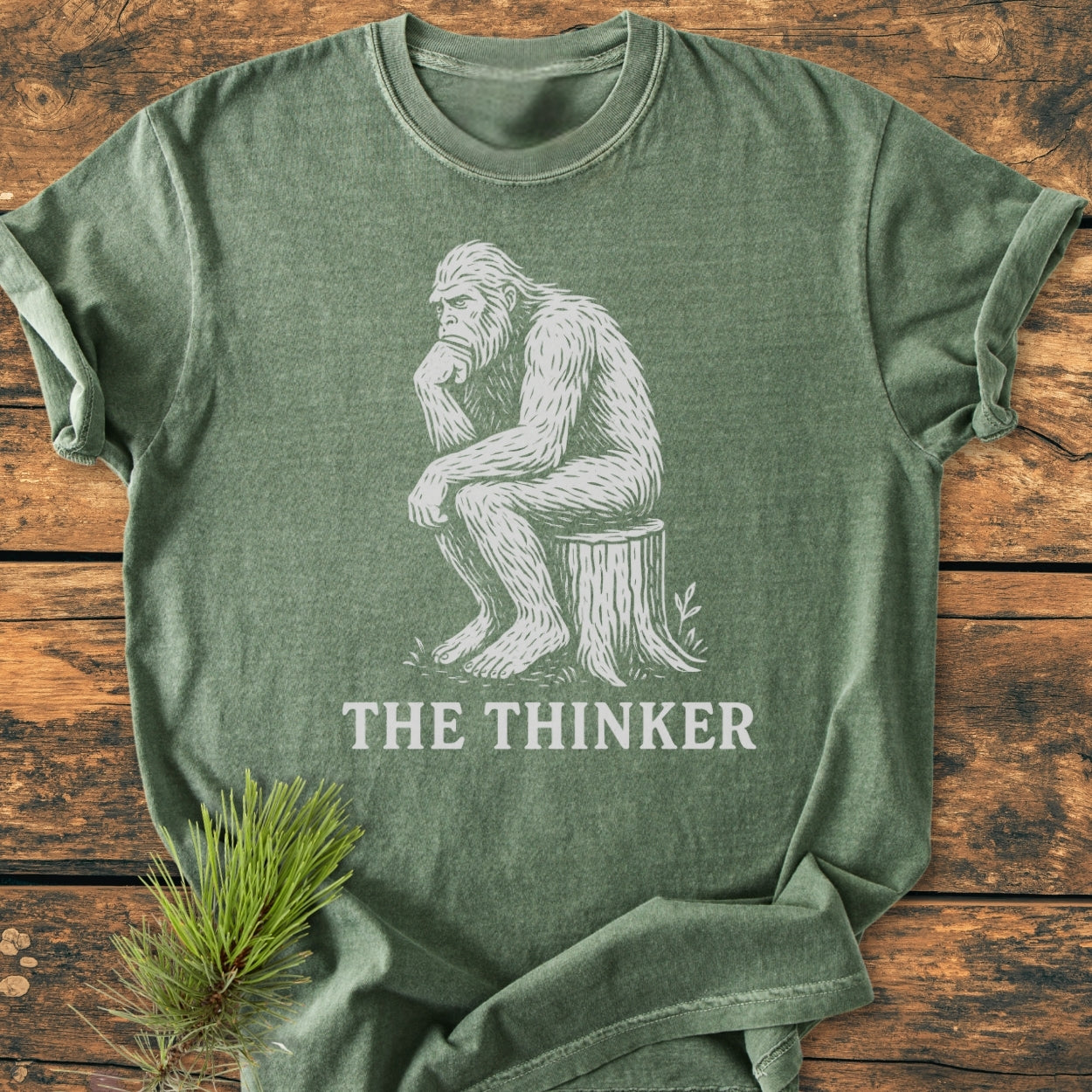 Bigfoot The Thinker - Vintage Wash Tee features a cartoon Bigfoot in Thinker pose on a green T-shirt, emphasizing comfort with its soft, garment-dyed fabric and relaxed fit.