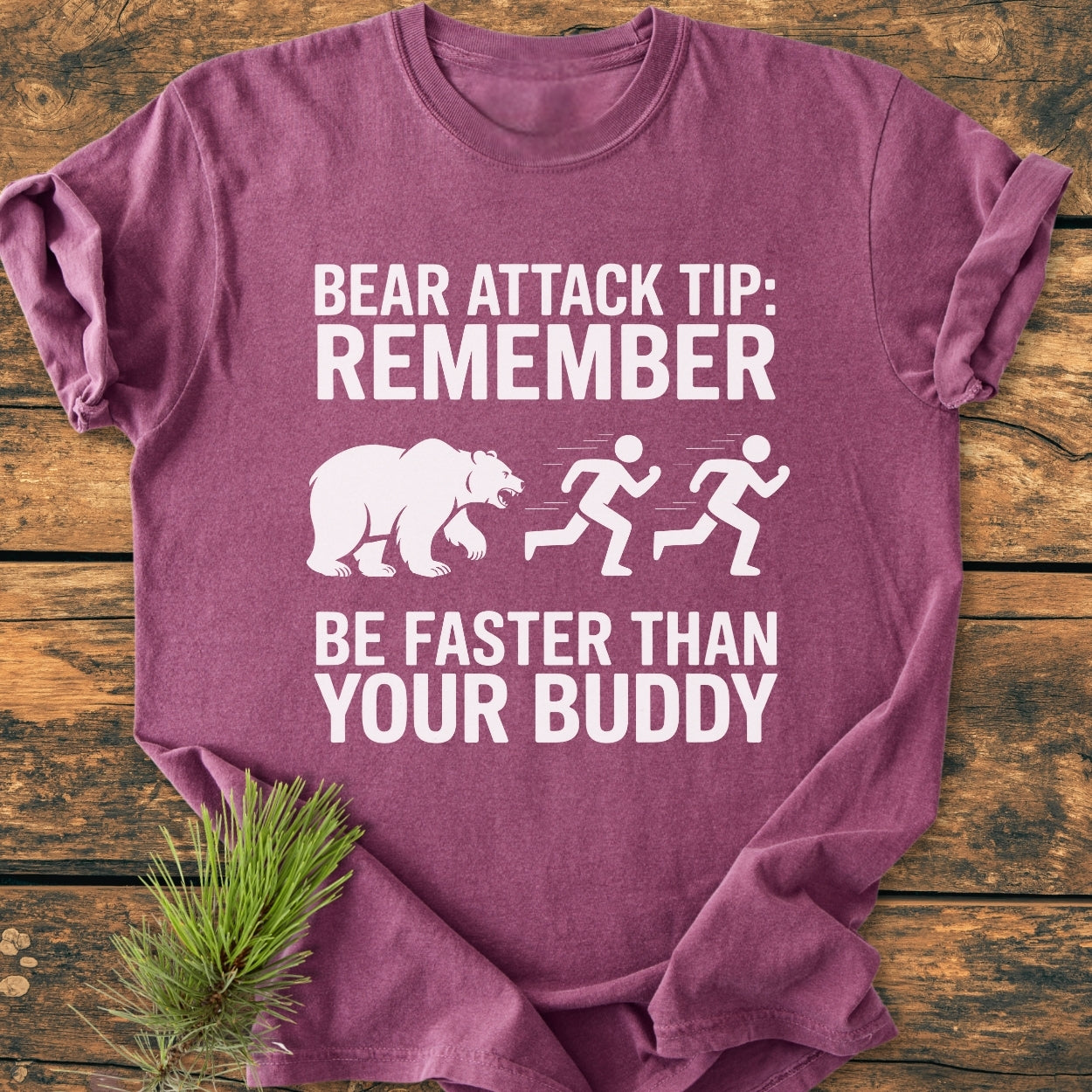Bear Attack Tip Be Fast - Vintage Wash Tee folded on wood, features humorous bear warning graphic. Soft, heather-purple, garment-dyed, 100% cotton, relaxed fit, with pine sprig accent.