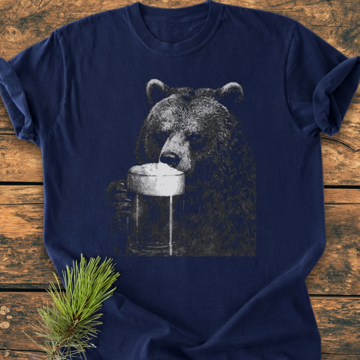 Grizzly With Beer - Vintage Wash Tee, featuring a bear drinking from a beer mug, laid flat on a table with a pine sprig, showcasing its relaxed fit and durable stitching.