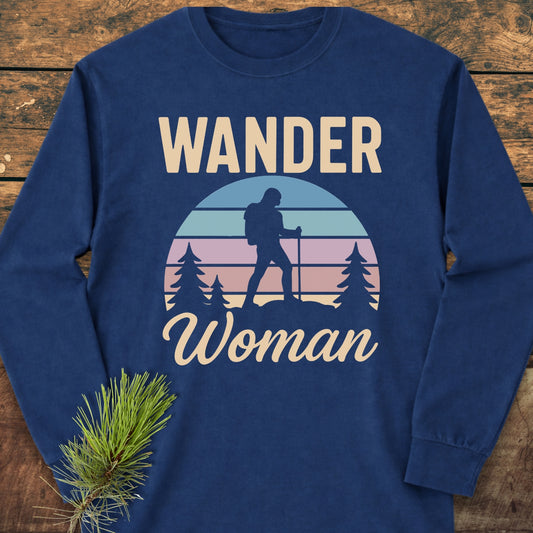 Wander Woman Retro Long-Sleeve Tee featuring a hiker graphic and pine trees on a navy-blue, cotton shirt, styled with a relaxed fit and soft garment-dyed fabric, laid on a wooden surface.