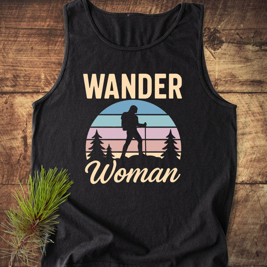 Wander Woman Retro Tank Top with a sleeveless design, featuring a graphic of a sunset, hiker, and trees, laid flat on wood with a pine sprig accent, emphasizing an outdoorsy theme.