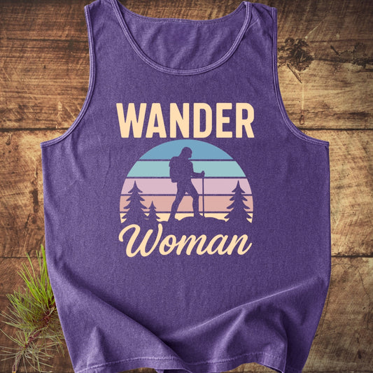 Wander Woman Retro Tank Top featuring a lone hiker graphic against a pastel sunset, laid on wood. Made from 100% US cotton, offering relaxed fit and sustainable materials.