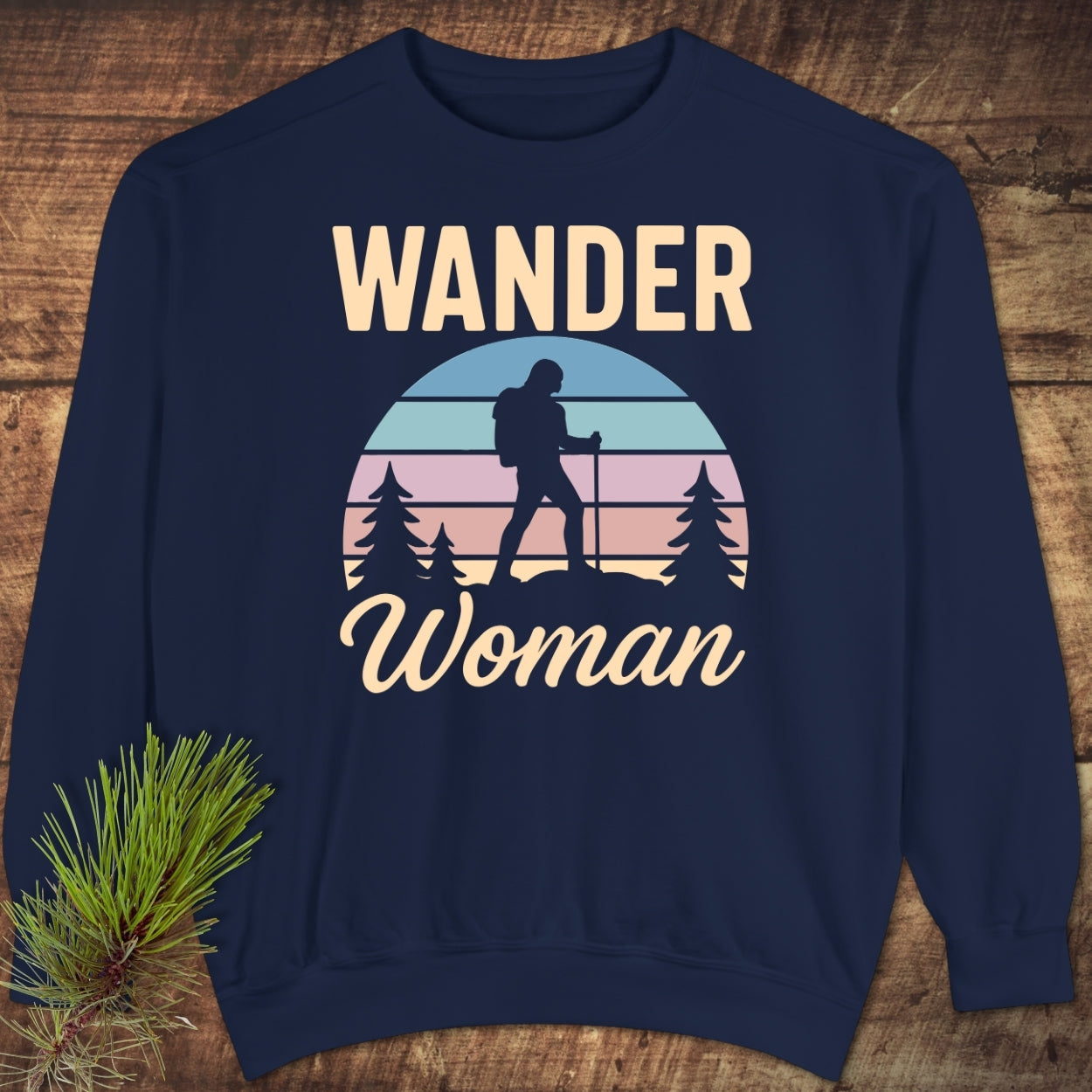 Wander Woman Retro Sweatshirt with bold WANDER text, pastel-striped circle featuring hiker silhouette among pine trees, and Woman in cursive. Navy-blue, laid flat, showcasing relaxed fit and quality fabric.
