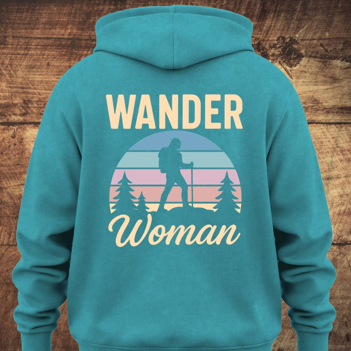 Back view of the Wander Woman Retro Hoodie BACKPRINT featuring WANDER text, pastel striped sunset motif with a woman hiker silhouette among pine trees, and Woman. in script below.