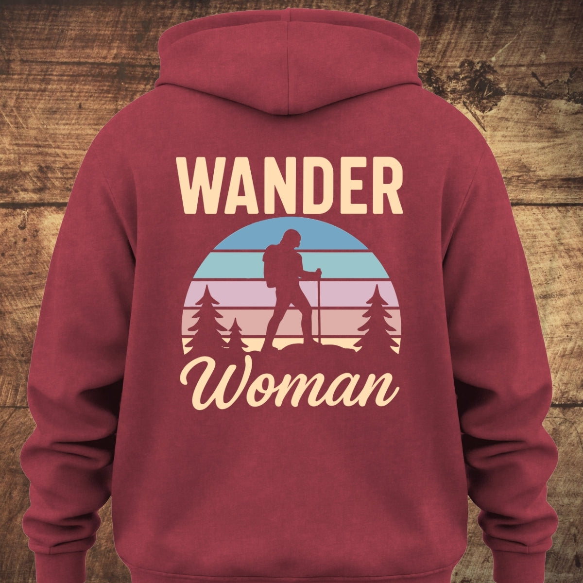 Back view of the Wander Woman Retro Hoodie BACKPRINT, featuring a circular sunset scene with pine trees and a woman hiker silhouette, surrounded by the words “WANDER Woman.” Perfect for trail mornings and cozy nights.
