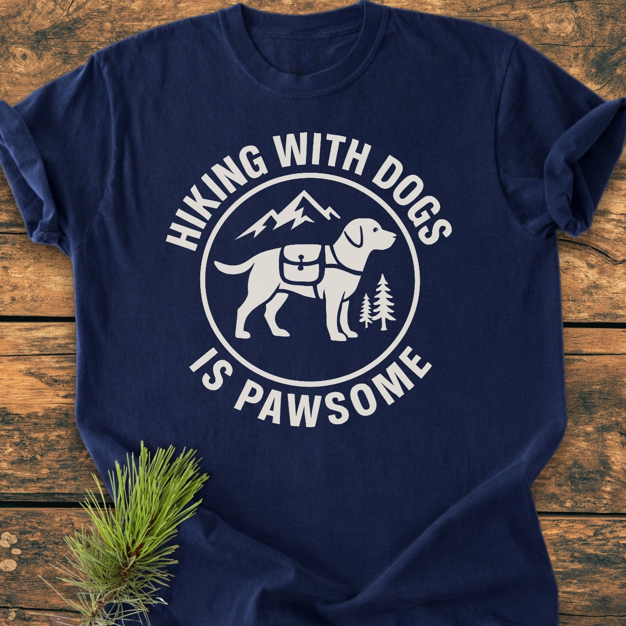Hiking With Dogs Is Pawsome - Vintage Wash Tee features a circular graphic of a dog with a hiking pack, mountains, and pine trees, showcasing Hiking with dogs is pawsome slogan on navy-blue fabric.