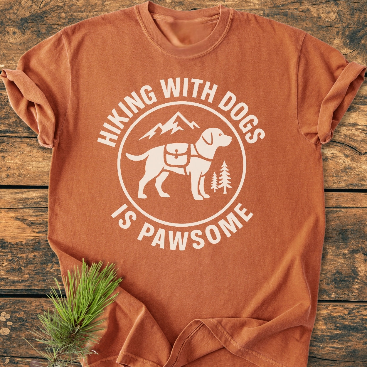 Hiking With Dogs Is Pawsome - Vintage Wash Tee showcasing a white graphic of a backpacked dog with mountains, laid flat with pine needles on soft, garment-dyed cotton for a relaxed daily fit.