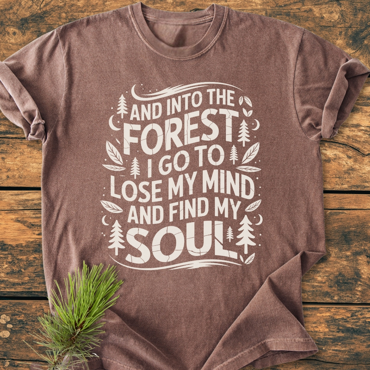And Into The Forest I Go - Vintage Wash Tee, featuring off-white forest-themed graphics and quote, laid flat on rustic wood. Made from soft, durable 100% ring-spun cotton for cozy, relaxed wear.