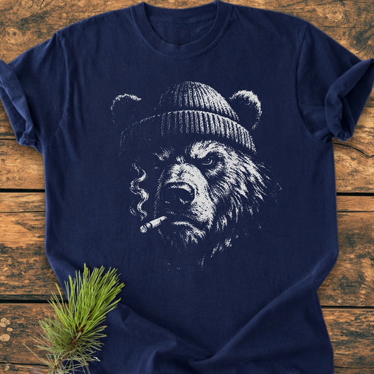Smoking Bear - Vintage Wash Tee: Navy-blue T-shirt featuring a sketched grizzly bear with a beanie and cigarette. Laid on wood with a spruce twig beside. Made from soft-washed, pre-shrunk ring-spun cotton.