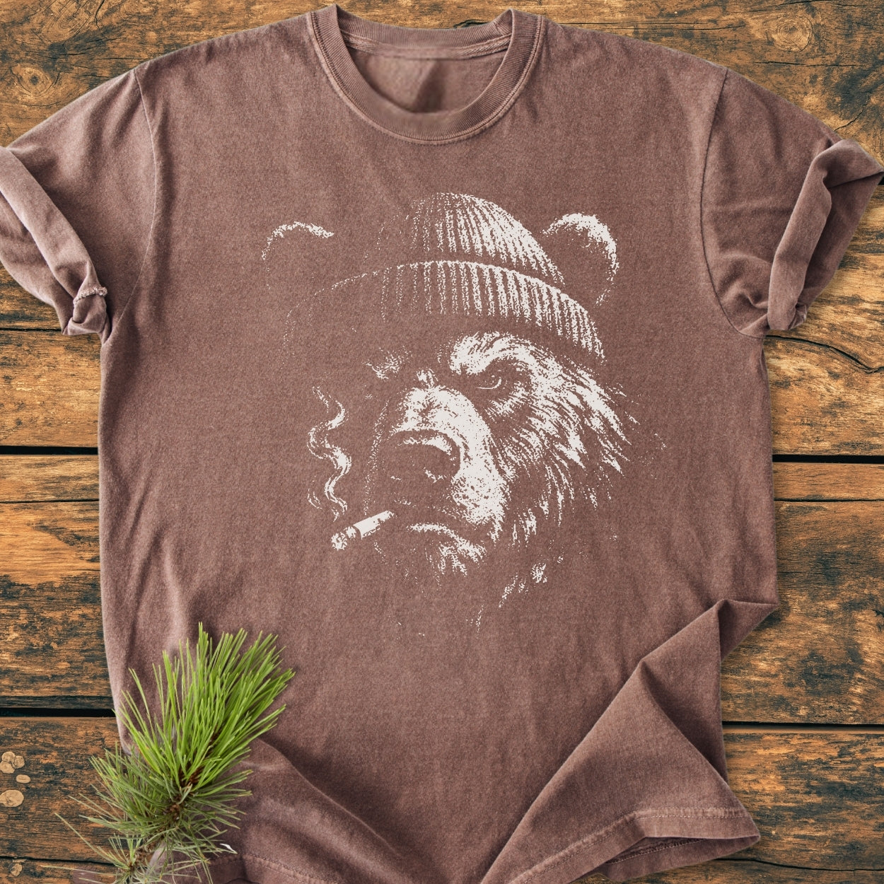Smoking Bear - Vintage Wash Tee featuring a bear with a beanie and cigarette in distressed white ink on a soft, brown, garment-dyed T-shirt, styled with a pine sprig accent.