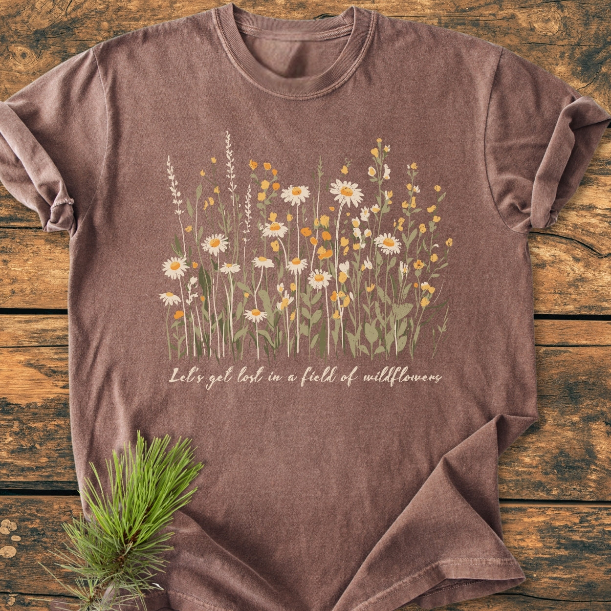Let's Get Lost In A Field Of Wildflowers - Vintage Wash Tee features daisies and yellow wildflowers on heather brown fabric, styled with a pine sprig. Relaxed fit, soft-washed, durable Comfort Colors 1717.