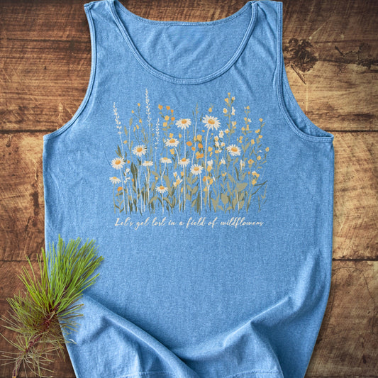 Let's Get Lost In A Field Of Wildflowers Tank Top, featuring a wildflower print and script on light-blue fabric, laid flat with a pine sprig, highlighting its relaxed fit and sustainable cotton material.
