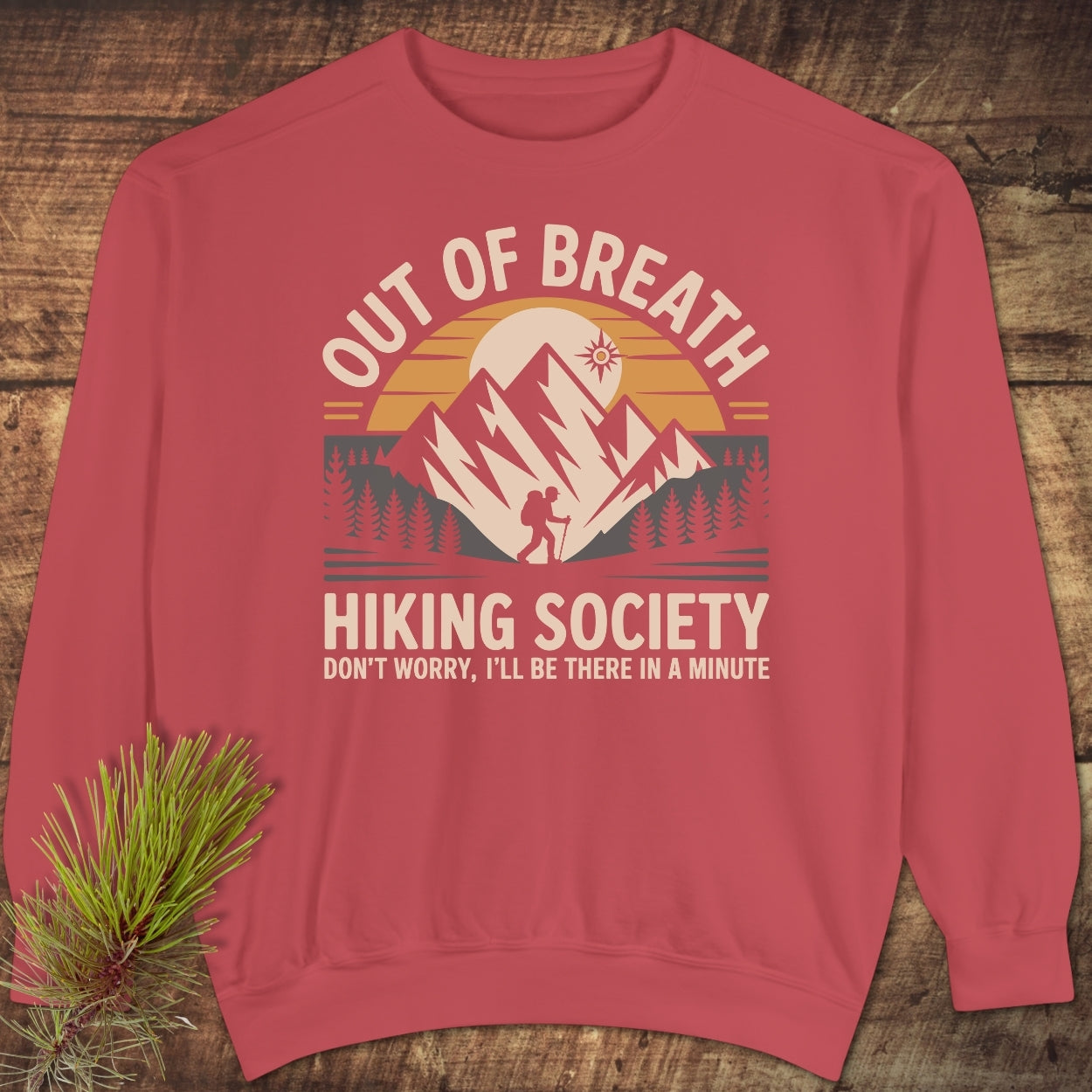 Out Of Breath Hiking Society Sweatshirt features a mountain graphic with a hiker, sun, and pine trees. Laid flat, this casual unisex sweatshirt exudes comfort with a relaxed fit and detailed design.