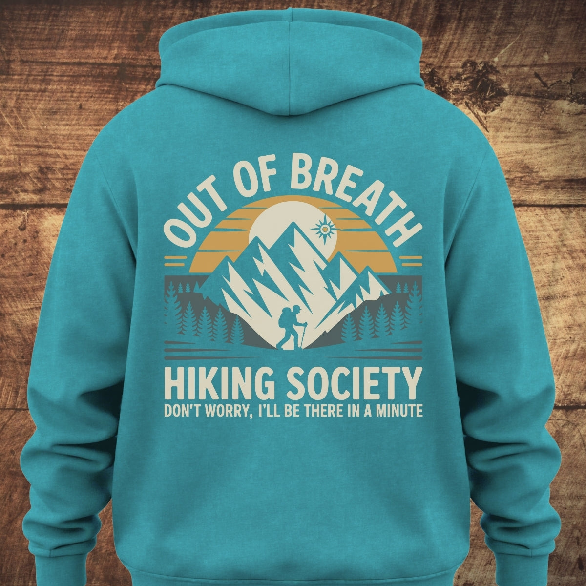 Out Of Breath Hiking Society BACKPRINT hoodie with a sunrise mountain design, featuring a lone hiker and pine trees, slogan DON’T WORRY, I’LL BE THERE IN A MINUTE, on soft, garment-dyed fabric.