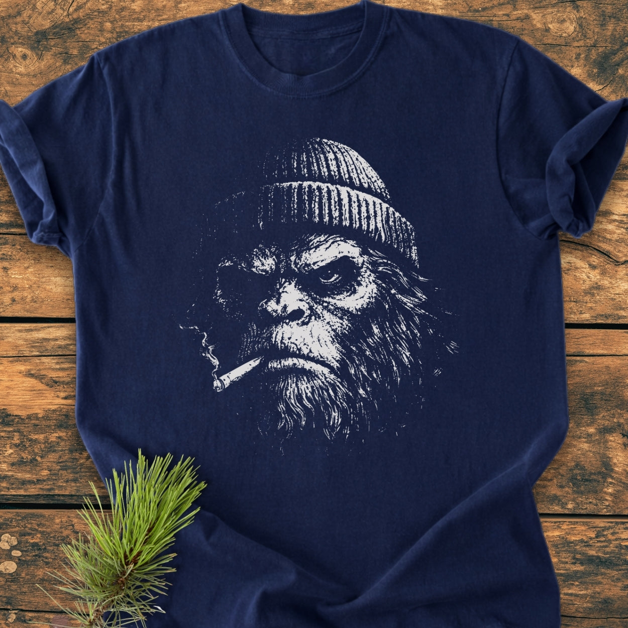 Slow Burn Club - Vintage Wash Tee features a sketch-style bearded ape face with a knit cap and cigarette, printed on a soft, navy-blue garment-dyed T-shirt, laid on a wooden surface.