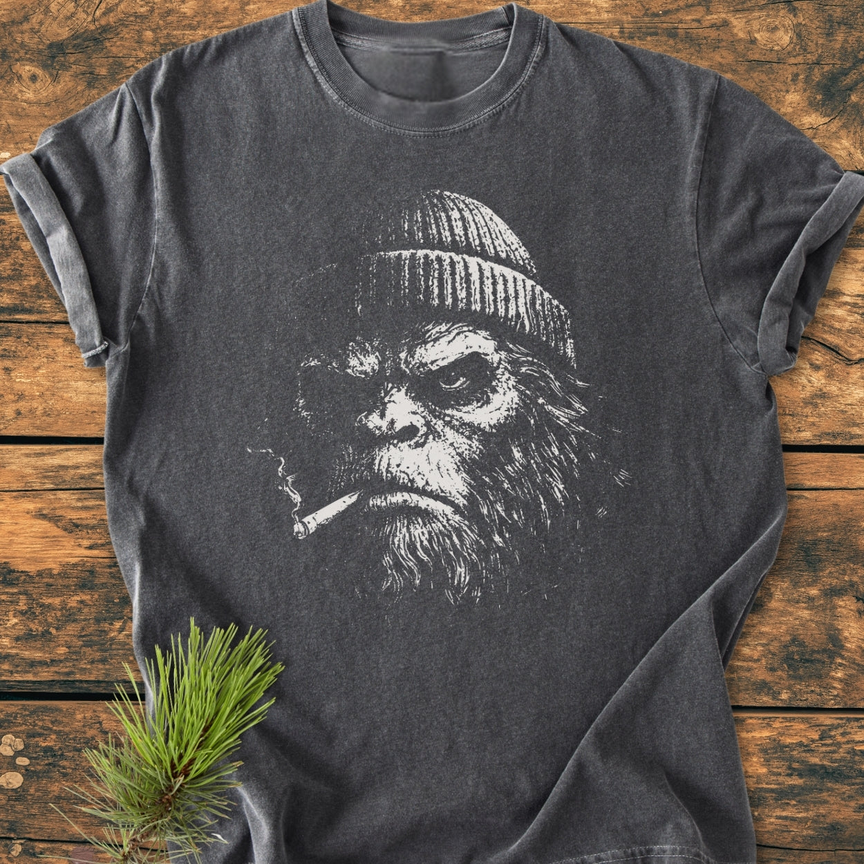 Slow Burn Club - Vintage Wash Tee features a sketch-style portrait of a bearded ape with a beanie, smoking. Laid on wood with a pine sprig, this dark gray, relaxed-fit tee offers exceptional comfort.