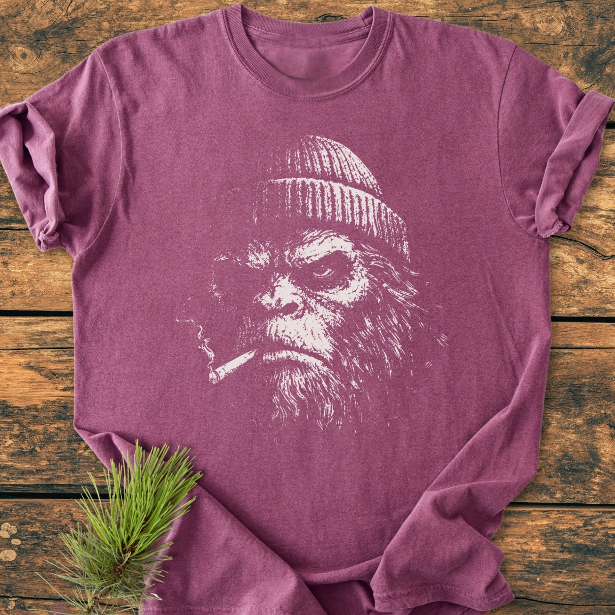 Slow Burn Club - Vintage Wash Tee features an angry bearded ape print, knit cap, cigarette. Heathered maroon, 100% ring-spun cotton, relaxed fit, styled with pine sprig on rustic wood background.