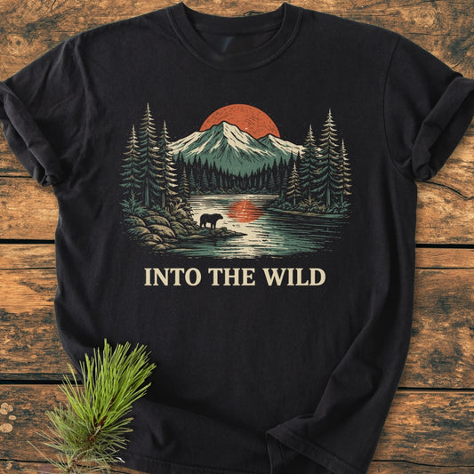Into The Wild - Vintage Wash Tee features a nature scene with mountains, evergreen trees, and a bear by a lake. Crafted from soft, durable 100% cotton, offering comfort and a relaxed fit.
