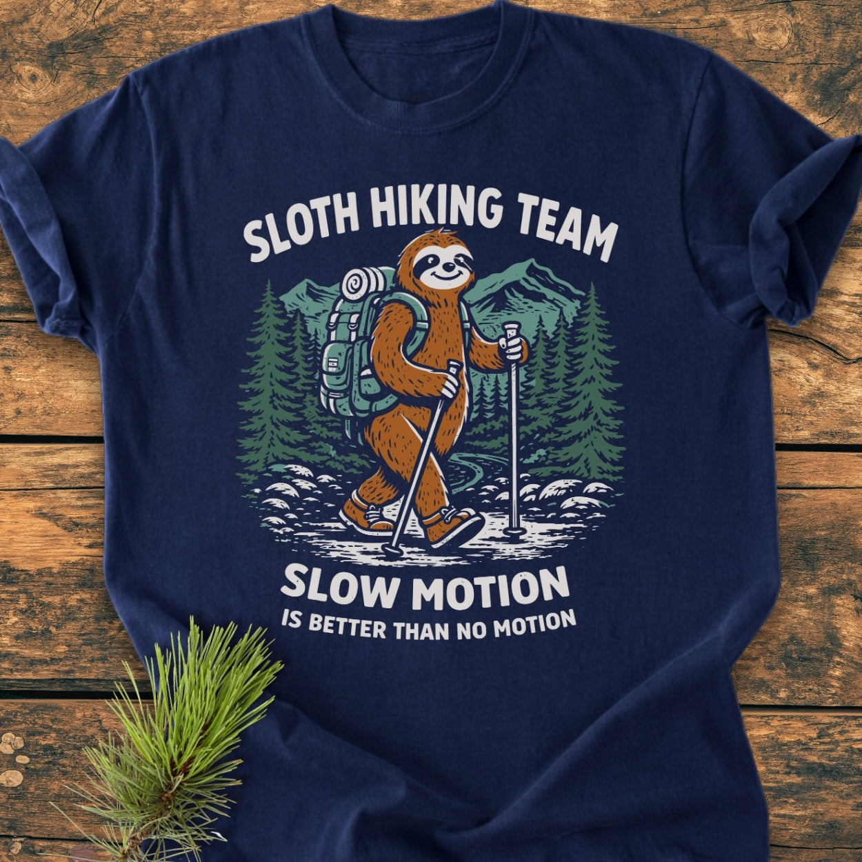 Sloth Hiking Team - Vintage Wash Tee: Navy-blue shirt featuring a cartoon sloth in hiking gear on a trail, with SLOTH HIKING TEAM and SLOW MOTION IS BETTER THAN NO MOTION slogans, laid on wooden surface.