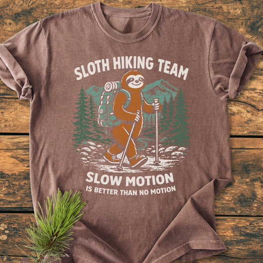 Sloth Hiking Team - Vintage Wash Tee featuring a cartoon sloth in hiking gear with the phrase Slow Motion Is Better Than No Motion, laid on a wooden surface, showcasing its relaxed fit and durability.