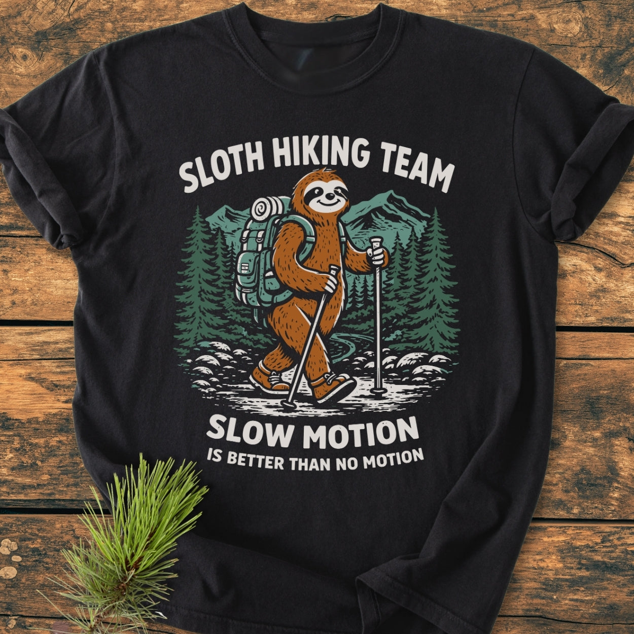 Sloth Hiking Team - Vintage Wash Tee features a cartoon sloth in hiking gear with trekking poles, amidst mountains and pine trees, on a black T-shirt. Text reads, “SLOW MOTION IS BETTER THAN NO MOTION.”