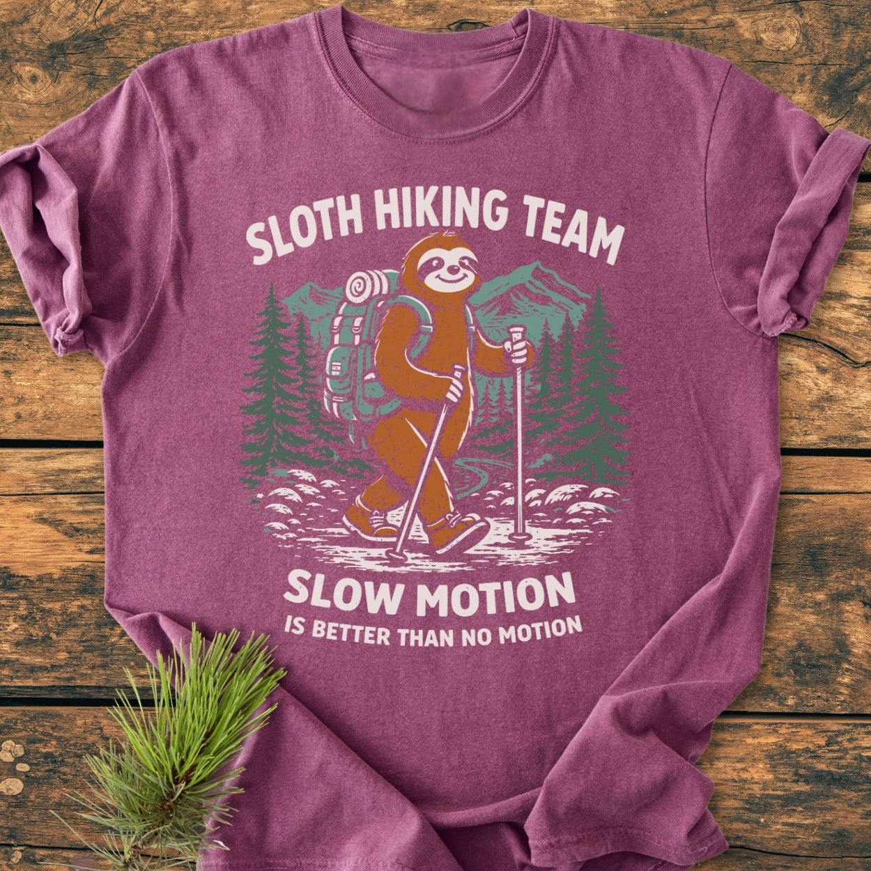 Sloth Hiking Team - Vintage Wash Tee featuring a cartoon sloth hiking scene. The heather-purple t-shirt lies on wood, showcasing its soft texture and relaxed fit, perfect for casual wear.