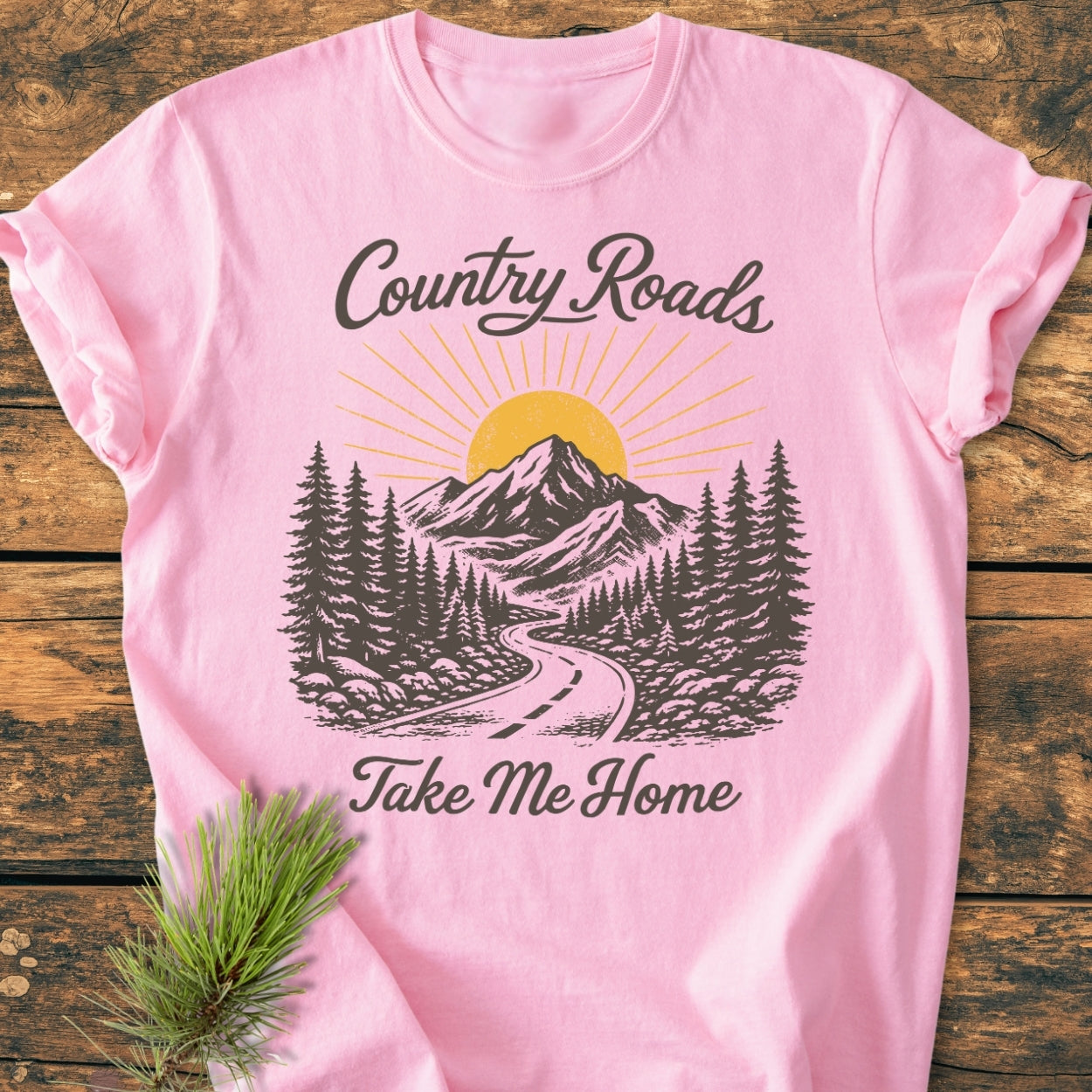 Country Roads - Vintage Wash Tee features a pink shirt with a country road scene and slogans. It's made of soft, garment-dyed 100% ring-spun cotton, offering a relaxed fit and durable stitching.