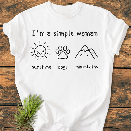 I'm A Simple Woman - Sunshine, Dogs, Mountains - Vintage Wash Tee displayed on wood with pine sprig; features phrase and icons of sun, dog paw, and mountain. Made from soft, durable, garment-dyed cotton.