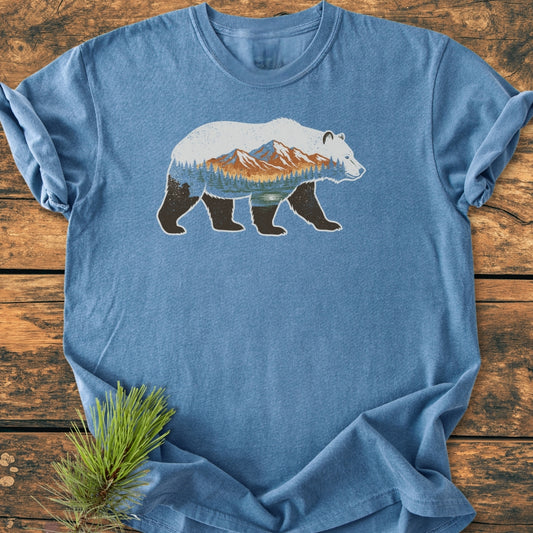 Mountain Within - Vintage Wash Tee features a large bear graphic with a landscape of pine trees, mountains, and lake on a heather-blue crew neck T-shirt, styled with a pine sprig.