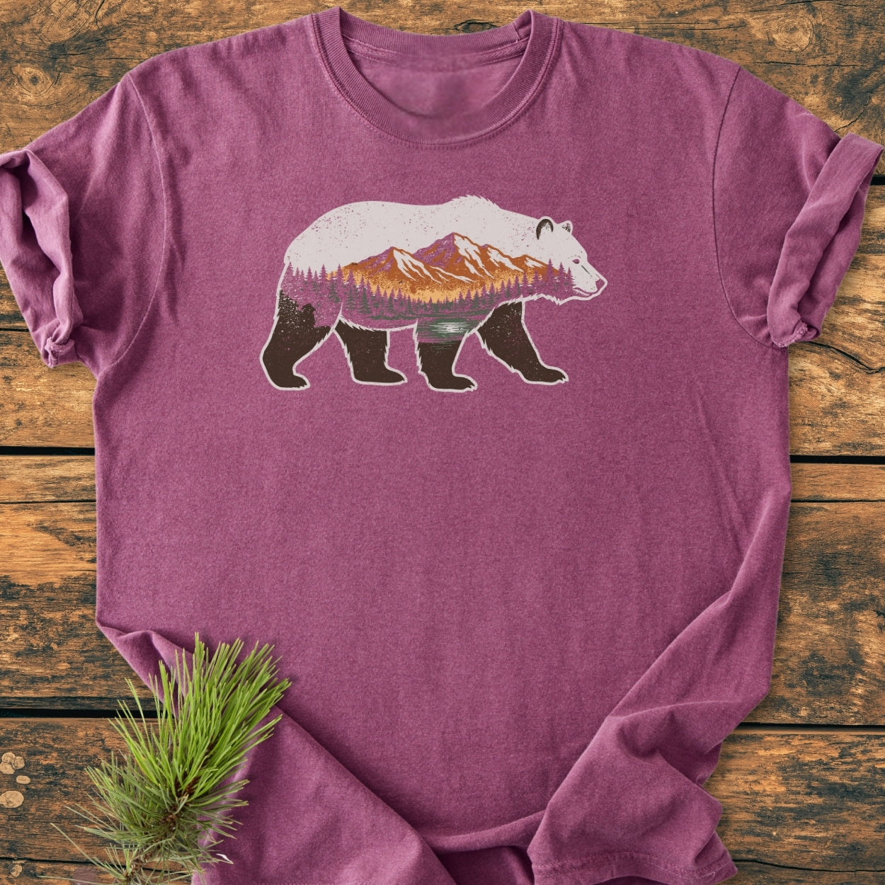 Mountain Within - Vintage Wash Tee featuring a bear silhouette with a mountain-and-forest scene, displayed on rustic wood. The tee is soft-washed, 100% ring-spun cotton, offering comfort and durability.