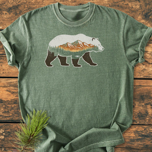 Mountain Within - Vintage Wash Tee featuring a bear silhouette with a pine and mountain landscape, laid flat on a wood-grain background, emphasizing its relaxed fit and durable, soft-washed fabric.