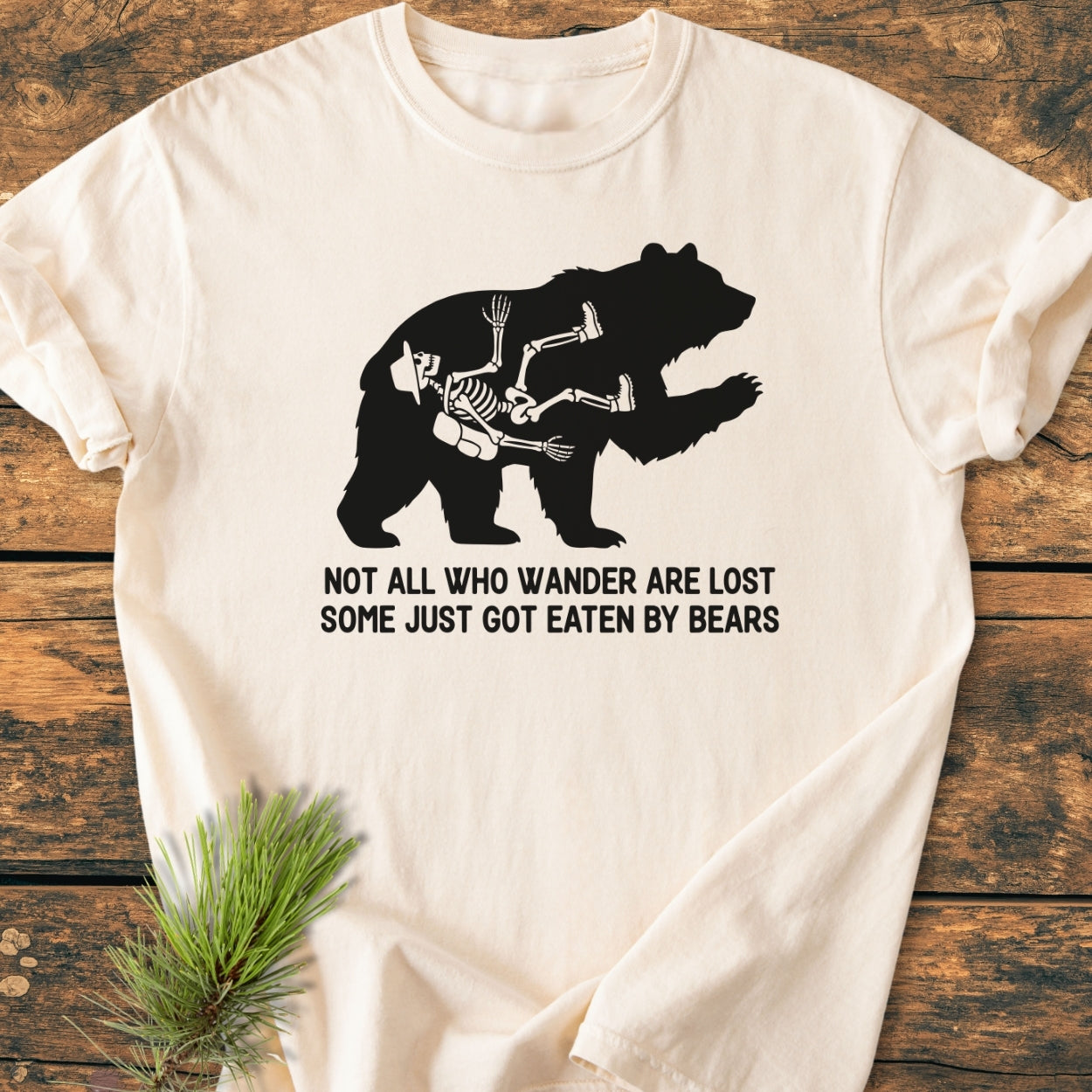 Not All Who Wander Are Lost - Vintage Wash Tee on rustic wood surface, featuring a black bear silhouette with a hiker's skeleton inside, and humorous text below. Made from soft, durable, 100% ring-spun cotton.