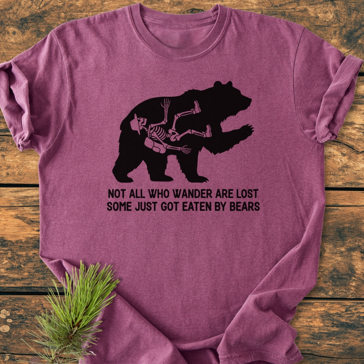 Not All Who Wander Are Lost - Vintage Wash Tee featuring a bear silhouette with a hiker's skeleton inside, laid on wood. Offers durable, soft-washed, garment-dyed fabric for comfort and a relaxed fit.