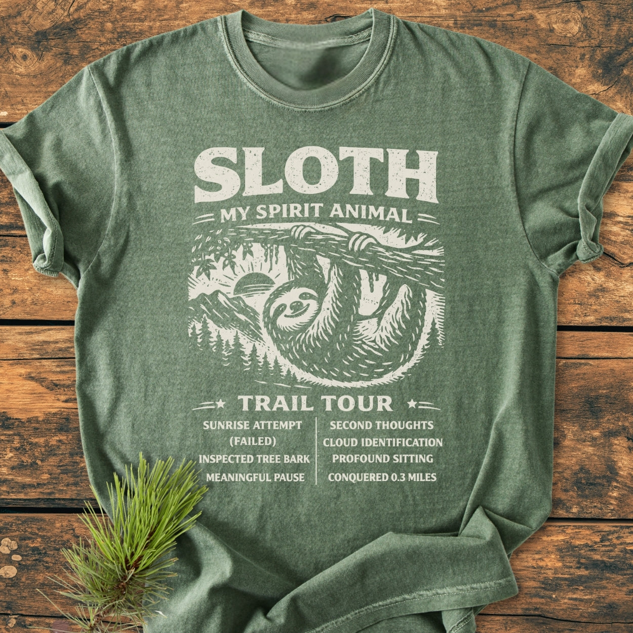 Sloth Spirit Animal Tour - Vintage Wash Tee features a stylized sloth design with humorous tour stops, laid flat on wood, showcasing its relaxed fit, durable double-needle stitching, and soft, pre-shrunk cotton.