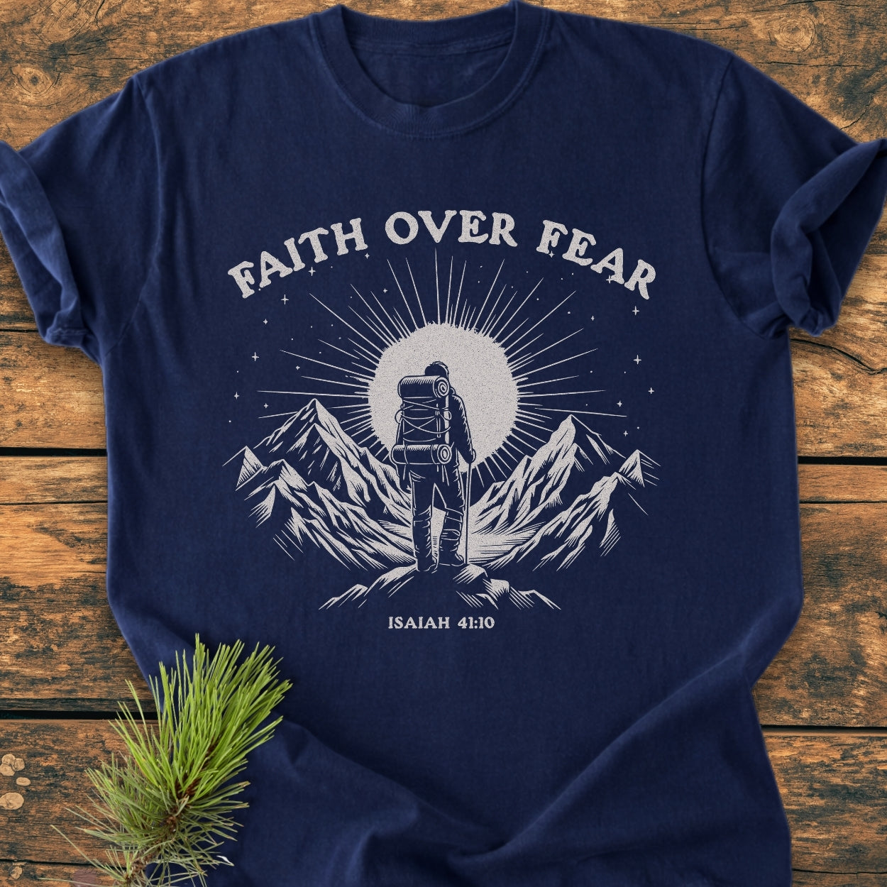 Faith Over Fear - Vintage Wash Tee, featuring a white graphic of a backpacker and mountains with ISAIAH 41:10 on a navy garment-dyed, soft-washed cotton, laid on rustic wood.