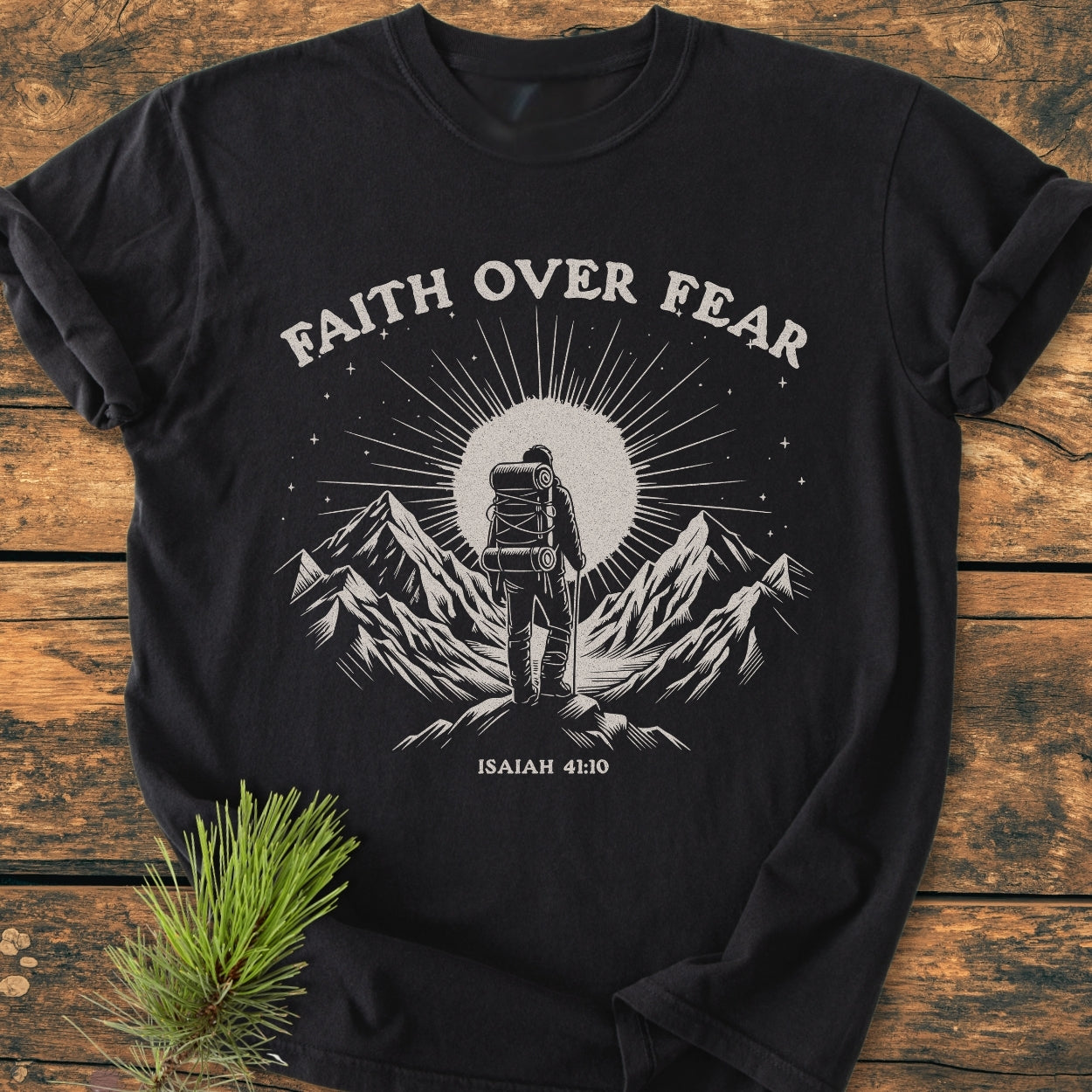Faith Over Fear - Vintage Wash Tee featuring a hiker illustration and scripture on a black tee, displayed on a wooden surface with a pine sprig, showcasing a cozy, relaxed fit.