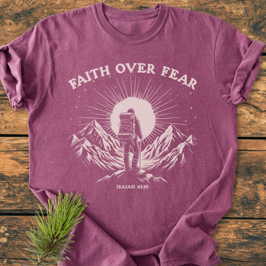 Faith Over Fear - Vintage Wash Tee in heather-purple, featuring a mountain scene with a backpacker and ISAIAH 41:10. Laid on wood with a pine sprig tucked underneath.