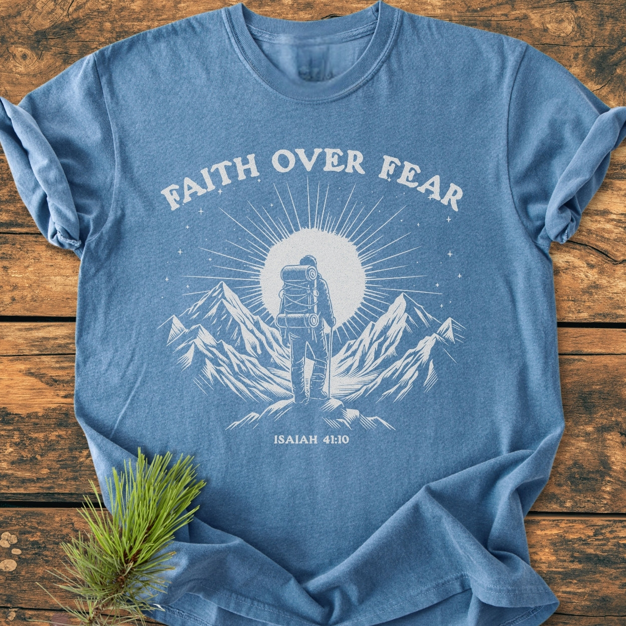 Faith Over Fear - Vintage Wash Tee features a stylized backpacker illustration with the slogan and scripture reference. Laid on wood, this heather-blue, soft-washed, relaxed-fit t-shirt exudes comfort and durability.