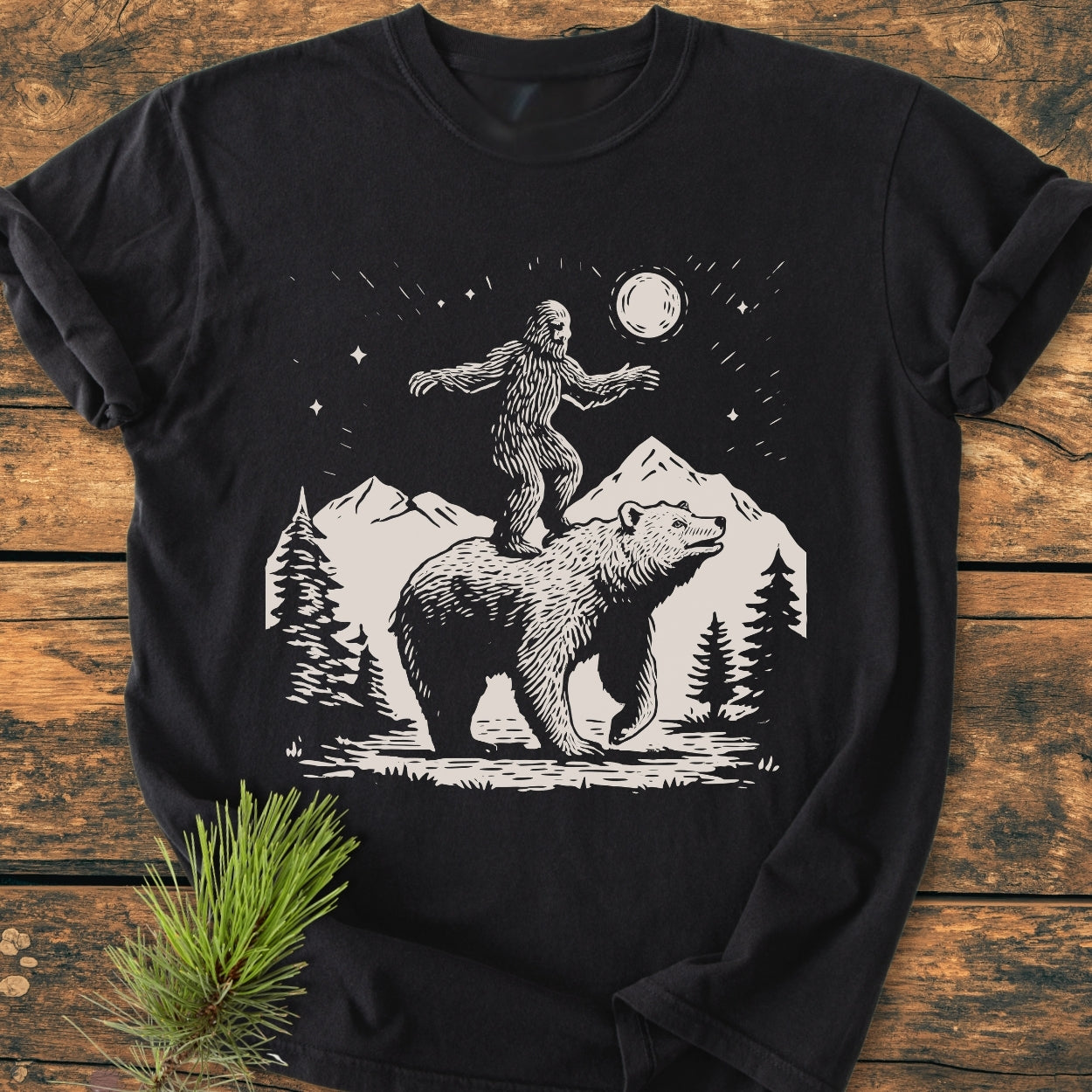 Bigfoot And Bear - Vintage Wash Tee features a black T-shirt with a stylized wilderness scene of a bear and Bigfoot under a starry sky, showcasing Comfort Colors' relaxed, durable, garment-dyed design.