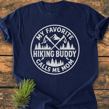 Navy-blue Hiking Buddy Mom - Vintage Wash Tee on wood surface, featuring white circular graphic with hiking poles, mountains, and trees, celebrating a mother’s hiking bond. Made from soft, durable, 100% ring-spun cotton.