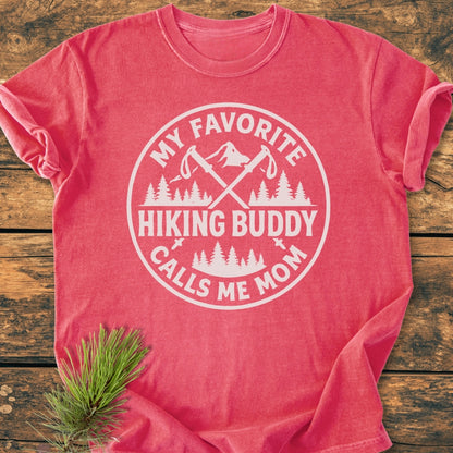 Hiking Buddy Mom - Vintage Wash Tee: A heathered red-coral T-shirt with a white graphic of trekking poles and mountains, slogan “My Favorite Hiking Buddy Calls Me Mom,” on rustic wood.