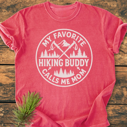 Hiking Buddy Mom - Vintage Wash Tee: A heathered red-coral T-shirt with a white graphic of trekking poles and mountains, slogan “My Favorite Hiking Buddy Calls Me Mom,” on rustic wood.