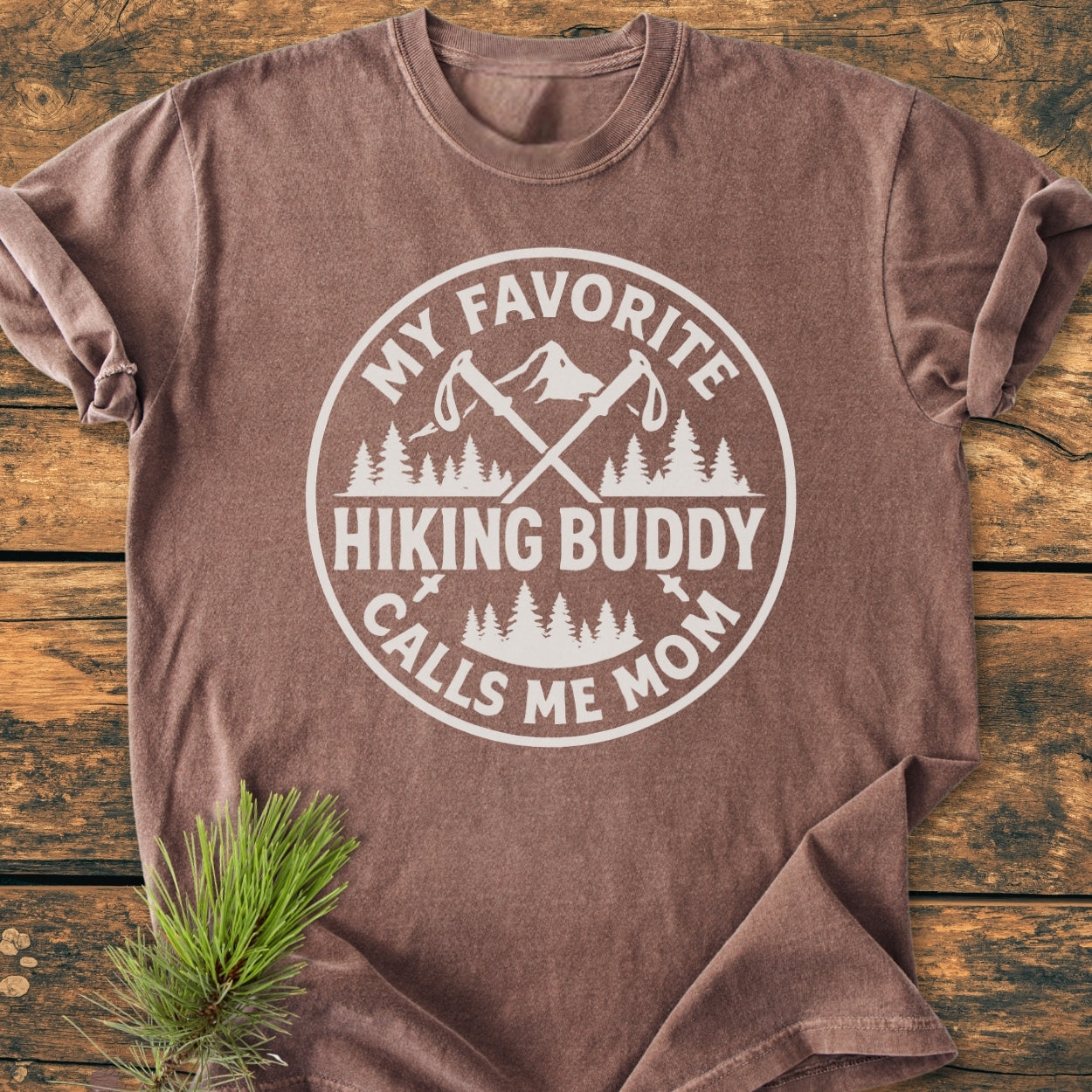 Hiking Buddy Mom - Vintage Wash Tee featuring a mountain graphic and phrase, laid flat on wood. Made from soft, pre-shrunk 100% ring-spun cotton, emphasizing comfort and durability.