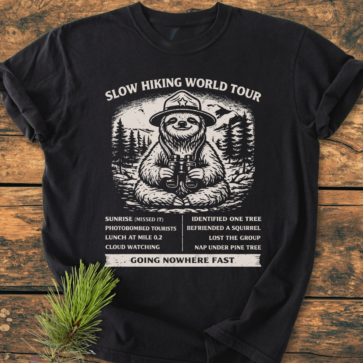 Slow Hiking World Tour - Vintage Wash Tee featuring a cartoon sloth in a ranger hat with binoculars, centered against pine trees, listing humorous hiking stops like Sunrise (Missed It) and Nap Under Pine Tree.