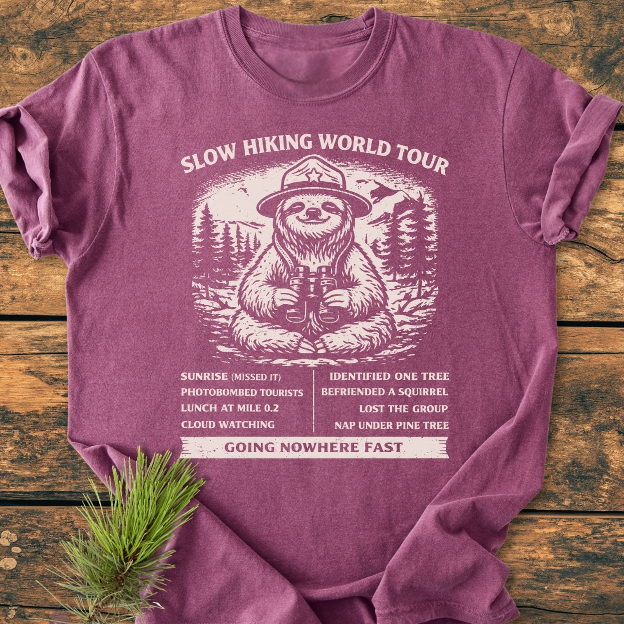 Slow Hiking World Tour - Vintage Wash Tee featuring a sloth with binoculars amid pine trees and mountains, highlighting a humorous hiking itinerary on a soft, relaxed-fit garment-dyed T-shirt.