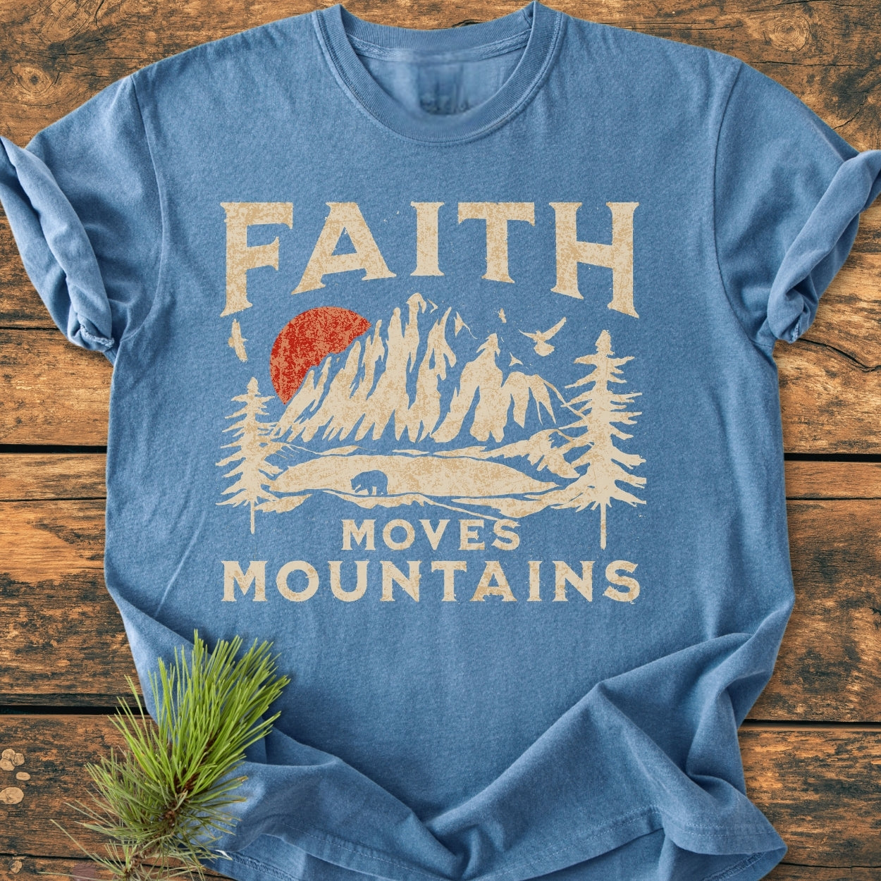 Faith Moves Mountains - Vintage Wash Tee features a mountain and pine tree graphic with a bear and sun, centered on a soft, heather-blue, garment-dyed, 100% cotton, relaxed fit T-shirt.