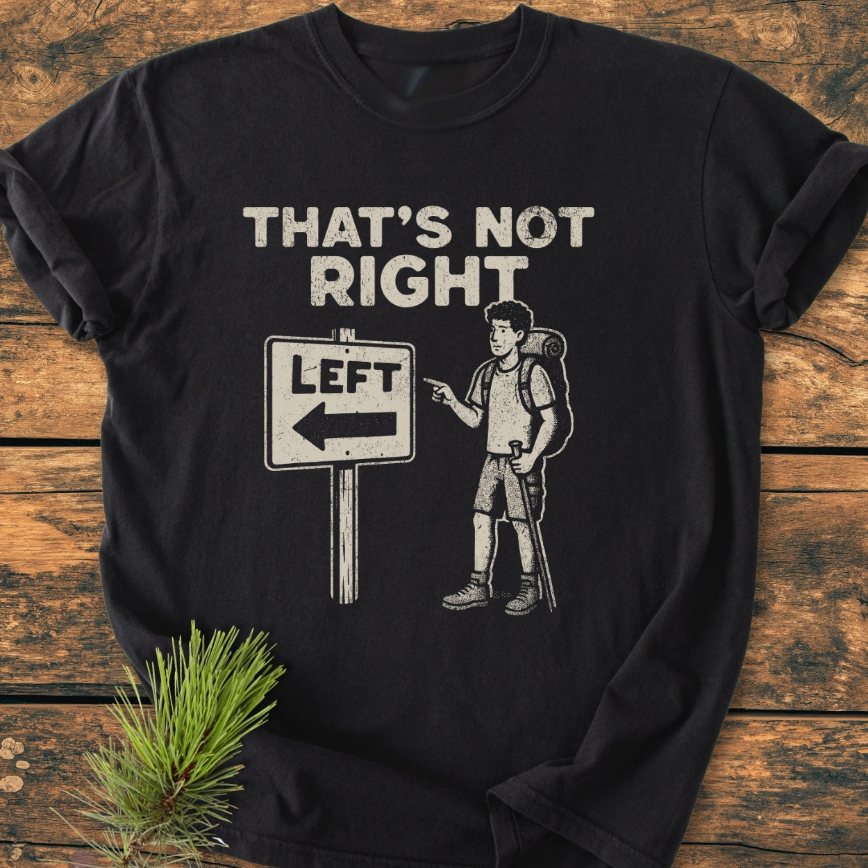 That's Not Right - Vintage Wash Tee features a whimsical design of a puzzled hiker by a 'LEFT' sign. Perfectly laid on a wooden surface, showcasing its relaxed fit and durable stitching.