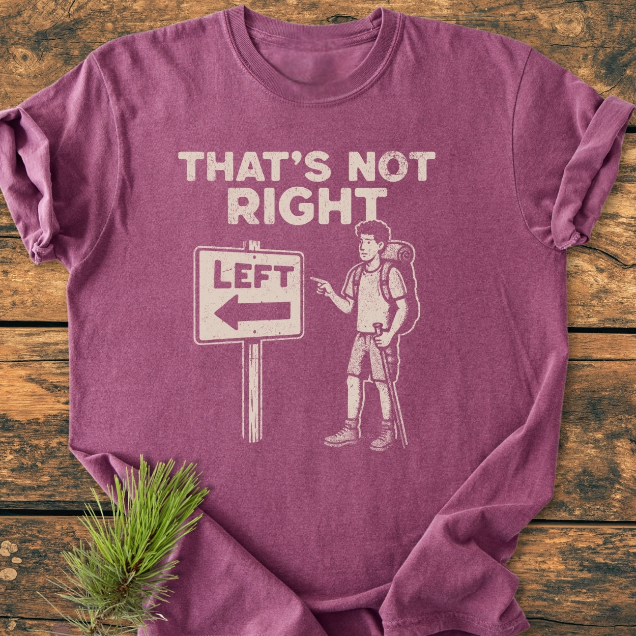That's Not Right - Vintage Wash Tee features a cartoon hiker with a road-sign pun on a maroon-toned, soft-washed fabric, laid on rustic wood, highlighting its cozy, relaxed fit and durable stitching.