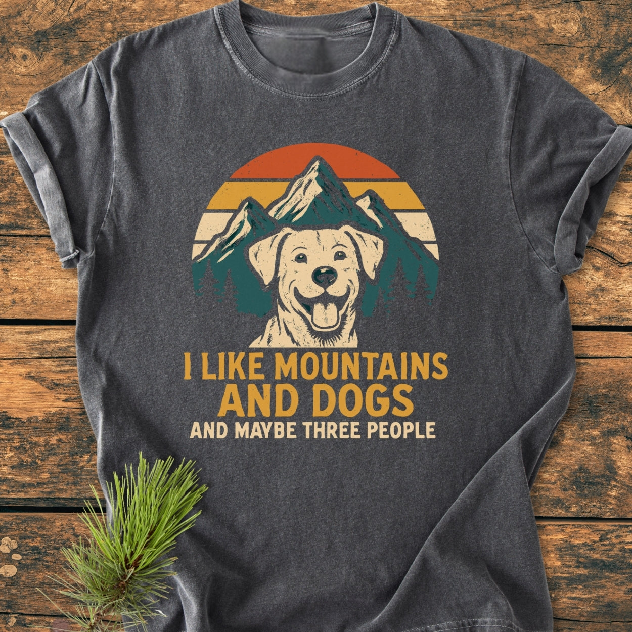 Charcoal-gray I Like Mountains And Dogs - Vintage Wash Tee featuring a happy dog graphic with a mountain sunset, bold slogan, and relaxed fit, laid on wood, highlighting its cozy, durable design.